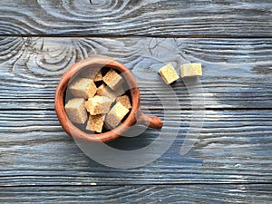 Pieces of brown sugar in a ceramic mug on a wooden background