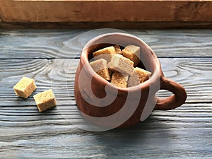Pieces of brown sugar in a ceramic mug on a wooden background