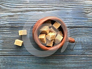 Pieces of brown sugar in a ceramic mug on a wooden background