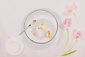 Pieces of cake on plate with fork, flowers and cup of milk on tabletop