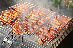 Pieces of chicken, squeezed between grill grates, frying on a grill brazier.