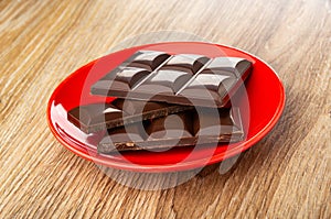 Pieces of chocolate bar in red saucer on table
