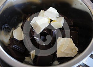 Pieces of chocolate and butter melt in a steel bowl. The process of making candy or dessert