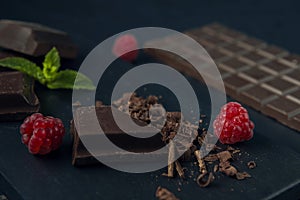 Pieces of chocolate, chocolate shavings, raspberry and mint on dark textured background