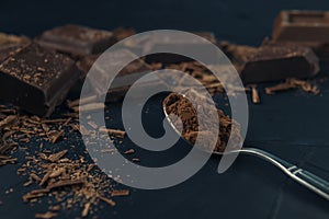 Pieces of chocolate, chocolate shavings and spoon with cocoa powder on dark blue textured background