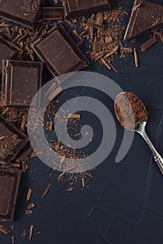 Pieces of chocolate, chocolate shavings and spoon with cocoa powder on dark blue textured background. Flat lay. Copy space