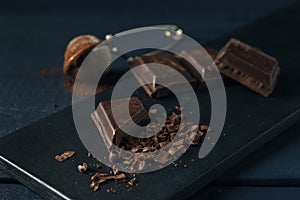 Pieces of chocolate, chocolate shavings and strainer with cocoa on dark wooden table