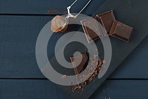 Pieces of chocolate, chocolate shavings and strainer with cocoa on dark wooden table. Top view. Copy space. Space for text