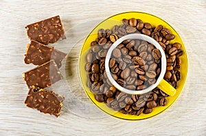 Pieces of chocolate, cup with coffee beans in saucer on wooden table. Top view