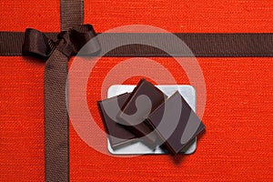 Pieces of chocolate on orange linen cloth with brown ribbon, closeup
