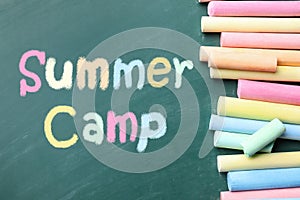 Pieces of color chalk and text SUMMER CAMP written on green chalkboard