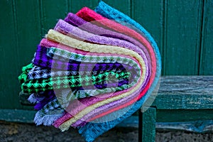 Colored woolen shawls in a pile on a wooden bench near the green wall