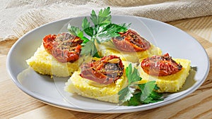 Pieces Corn polenta baked with cherry tomatoes, Parmesan cheese on the plate.
