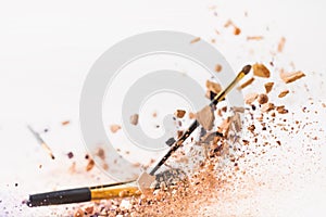 Pieces of cosmetic powder with makeup brushes falling