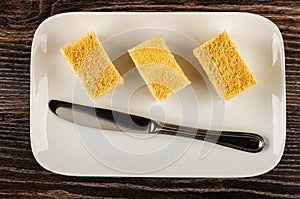 Pieces of cottage cheese and yogurt cake with shortcrust crumbs and knife in plate on wooden table. Top view