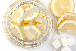 Pieces cut of lemon in a glass bowl and of sugar on a white background