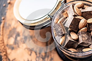 Pieces of dark bitter chocolate with cocoa and nuts almonds on wooden background. Concept of confectionery ingredients