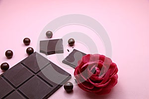 Pieces of dark chocolate bar and milk chocolate pearls and valentines rose on pink background, top view, copy space