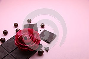 Pieces of dark chocolate bar and milk chocolate pearls and valentines rose on pink background, top view, copy space