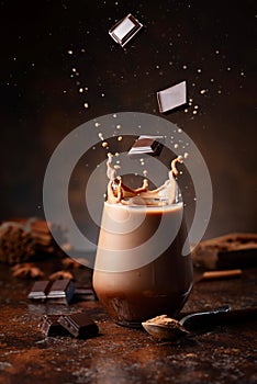 Pieces of dark chocolate fall into a glass of cocoa drink