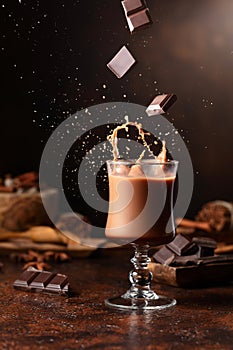 Pieces of dark chocolate fall into a glass of cocoa drink