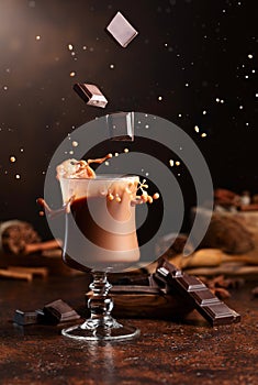 Pieces of dark chocolate fall into a glass of cocoa drink