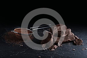 Pieces of dark chocolate and sieve with cocoa powder on table