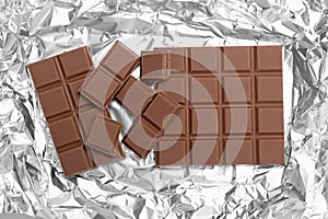 Pieces of delicious milk chocolate bars on foil, flat lay