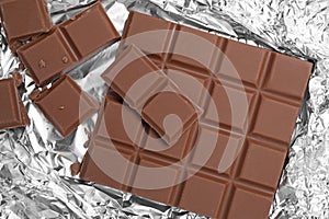 Pieces of delicious milk chocolate bars on foil, flat lay