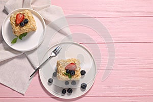 Pieces of delicious Napoleon cake with fresh berries served on pink wooden table, flat lay. Space for text