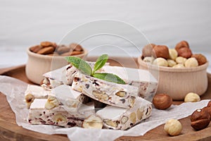 Pieces of delicious nougat and nuts on wooden board, closeup