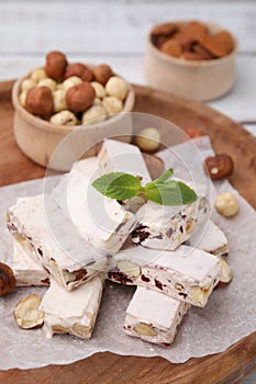 Pieces of delicious nougat and nuts on wooden board, closeup