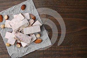 Pieces of delicious nutty nougat, hazelnuts and almonds on wooden table, top view. Space for text