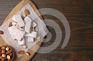 Pieces of delicious nutty nougat, hazelnuts and almonds on wooden table, top view. Space for text