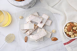 Pieces of delicious nutty nougat, nuts and honey on white table, flat lay