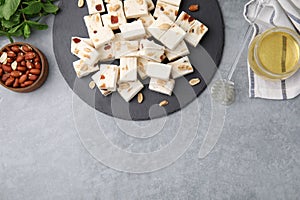 Pieces of delicious nutty nougat, peanuts and honey on light gray table, flat lay. Space for text