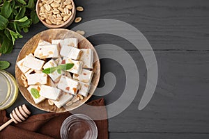 Pieces of delicious nutty nougat, peanuts, mint and honey on gray wooden table, flat lay. Space for text