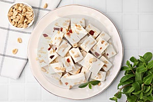 Pieces of delicious nutty nougat, peanuts and mint on white table, flat lay