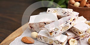 Pieces of delicious nutty nougat on table, closeup. Banner design