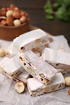 Pieces of delicious nutty nougat on white parchment paper, closeup