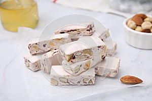 Pieces of delicious nutty nougat on white table, closeup