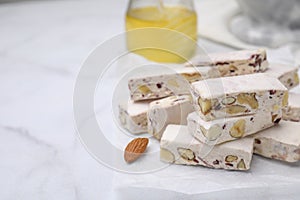 Pieces of delicious nutty nougat on white table, closeup. Space for text