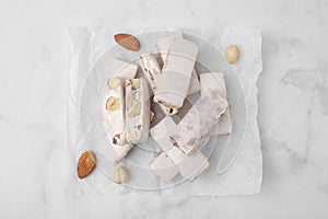 Pieces of delicious nutty nougat on white table, top view