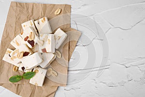 Pieces of delicious nutty nougat on white textured table, top view. Space for text
