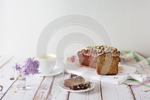 Pieces of delicious, sweet cupcake on white saucer, cup of tea, sprig of lilac on wooden background with linen napkin. Homemade