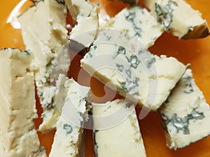 Pieces of dorblu cheese on an orange plate, close-up