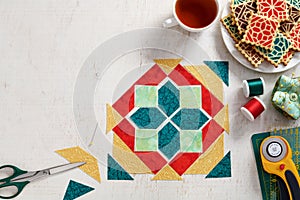 Pieces of fabric laid out in the shape of a patchwork block, a  heap of cookies with a pattern imitating a patchwork block, a cup