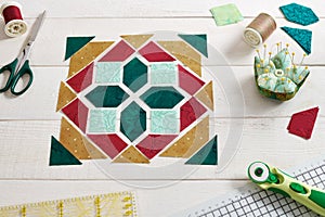 Pieces of fabric laid out in the shape of a patchwork block, sewing and quilting accessories. Traditional quilting