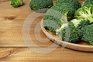 Pieces of fresh green broccoli on the plate on wooden table, copy space