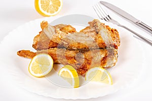 Pieces of fried fish and lemon on a white plate